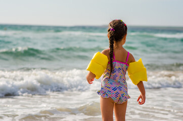 Girl 5 years old in a beautiful color in the arm ruffles swimsuit for swimming stands on the beach...