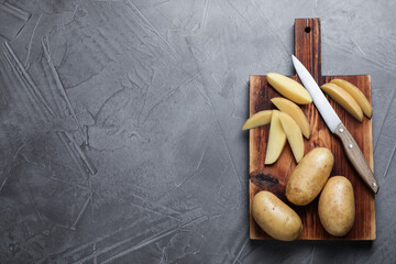 Raw potatoes, knife and wooden board on grey table, top view. Space for text