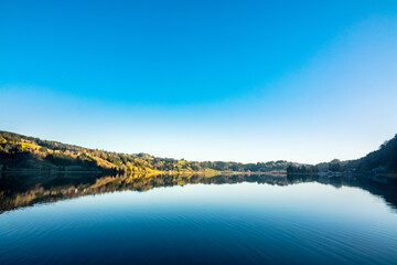 Fototapeta premium Blue sky and lake with trees on the shore reflected in the water, beautiful natural scenery