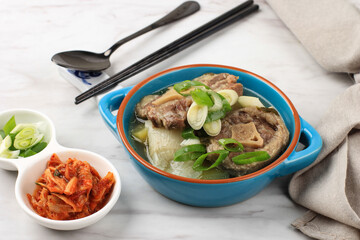 Close Up Gori Gomtang (Sokkori Gomtang) or Korean Beef Oxtail Stew  Soup, Served in the Blue Bowl with Kimchi and Sliced Green Onion