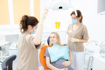 Young pregnant woman at the dental clinic, sitting in the treatment chair, the dentist and her...