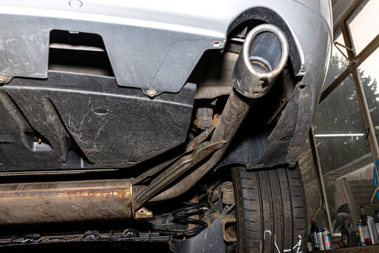 The exhaust system in the car seen from below, visible end silencer and wheel, the car is on the lift in the car workshop.