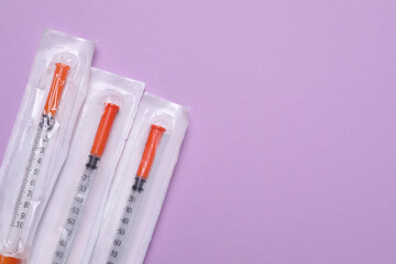 Packed disposable syringes on violet background, flat lay. Space for text