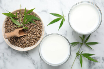 Hemp milk, seeds and fresh leaves on white marble table, flat lay