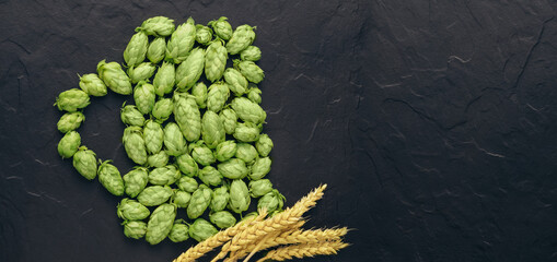 The green hop cones pattern in form of a pint of the beer and wheat ears on a black stone...
