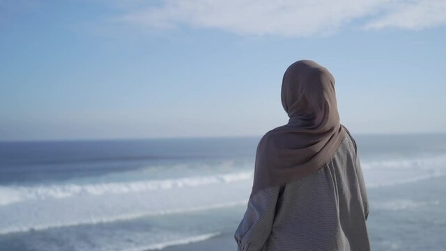 asian girl in hijab covering her head, smiling with happiness at the beach