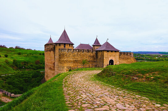 Khotyn, Ukraine-May 14, 2021:Classic wide-angle spring landscape view of medieval Khotyn castle with old cobblestone road against blue sky. Green hills in the background