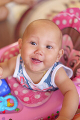 Asian infant baby boy sitting in a pink stroller is smiling and looking at the camera.