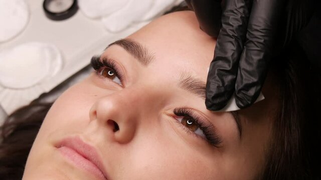 The master prepares the eyebrows by wiping them with a cotton swab before applying the microblading of the permanent makeup eyebrow tattoo