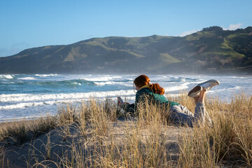 Red haired teen girl with her beloved pet - a retired New Zealand sheep dog - at the beach, taking selfies together. 