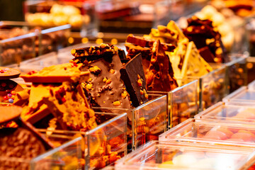 Different types of chocolate with almonds in glass display case, selective focus.