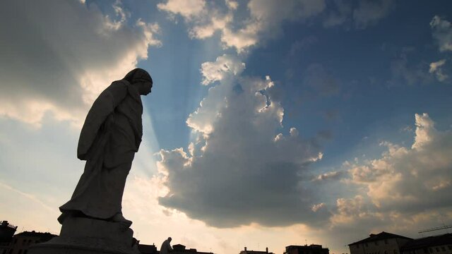 Epic clouds and sunset sky behind the silhouette of a religious stone statue. Beautiful and spiritual old monument of a Christian monk and philosopher in Italy. 4K.