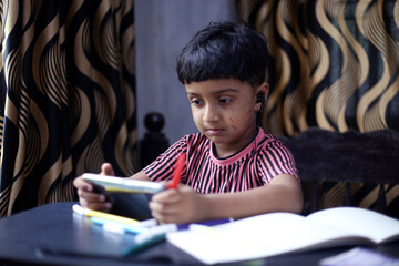 Asian kid attending online school using mobile phone, Online class concept Indian kid