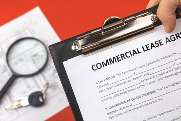 Man holds commercial lease agreement in hand. Clipboard with official document. Background with real property papers and house keys - obrazy, fototapety, plakaty