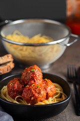 Meatballs with homemade tomato sauce  and spagetti in black ceramic bowl.Cooking traditional recipe.