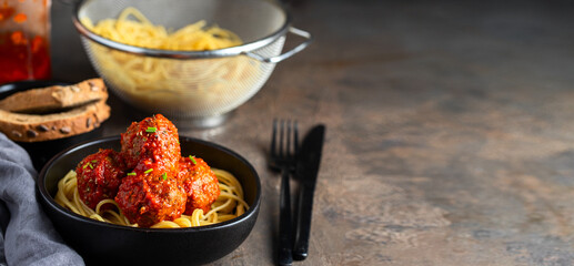 Italian Spaghetti and Meatballs with homemade tomato sauce in black ceramic bowl. Large inage for banner copy space.