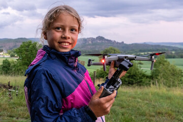 Porträt eines jungen, hübschen, nachdenklichen, blonden Mädchens mit startbereiter Drohne. Das Kind möchte ihre nähre Umgebung und die Natur aus der Luft entdecken und erkunden.