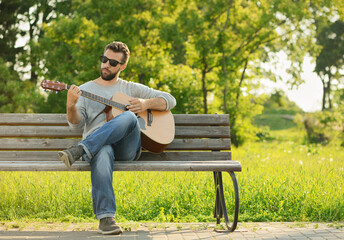 Caucasian man, 30 years old, is playing his classical guitar in park at sunset.