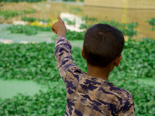 A indian boy pointing hand towards lake side, kids lifestyle concept image