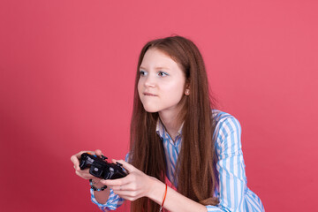 Little kid girl 13 years old in blue dress isolated on pink background holding joystick gaming...