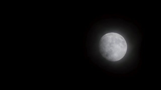 Full glowing mooon in cloudy night with slowly moving light clouds.