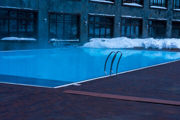 Swimming pool with blue warm water among snowdrifts near the hotel in winter
