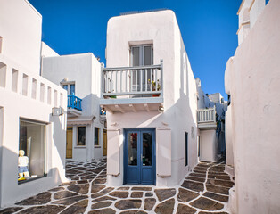 Traditional narrow cobbled streets, beautiful alleyways of Greek island town. Whitewashed houses, shop, cafe, morning summer sunshine. Mykonos, Greece