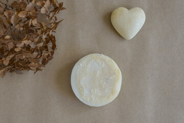 One piece of round natural handmade soap, dry flower of buldenezh and souvenir heart on craft paper.  Aromatherapy, skin care. Top view, flat lay. Copy space. Selective focus.