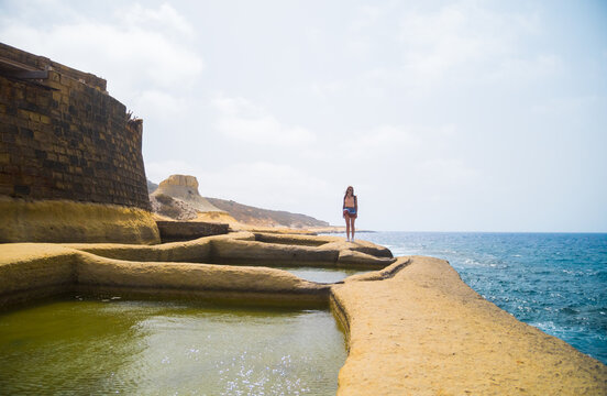 Lonely young woman walking or hiking the Mediterranean Salinas, Xwejni Salt Pans in Gozo in Malta.