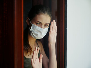 woman in medical mask sad look from the window prohibition