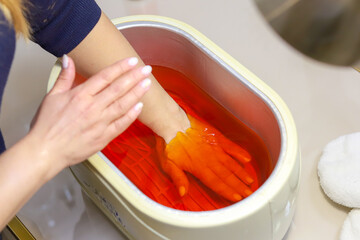 Paraffin theoraphy. Female hand and orange paraffin wax in bowl. Manicure and skincare. Woman girl in beauty spa salon.