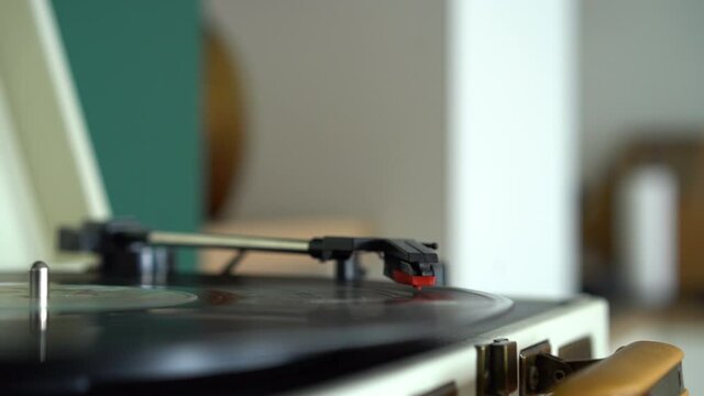 The needle rises from a vintage vinyl record. The vinyl record is spinning. The needle plays on a vintage vinyl record