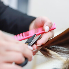 Stylist cutting split ends on her client at the salon. Close up. Square format.