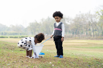 Happy African American little boy and girl holding dustpan and collecting trash into a bag. Group of Afro with hair curly volunteer charity environment outdoor in the park. Children playing outdoor