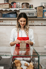 Beautiful young female seller working in a confectionery shop or bakery. She is selling and packing delicious sweets.