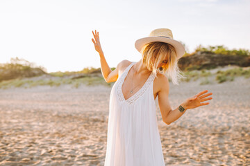 Happy young woman wearing white long dress and straw hat dance alone beach during dawn. Happiness, freedom