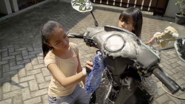 potrait happy young girl and little sister washing motorcycle at home