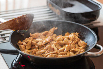 The cut chicken is wrapped in a mixture of spices and fried in a pan.