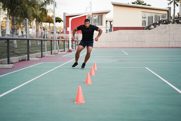 Hispanic man doing speed and agility cone drills workout session outdoors - Focus on man face