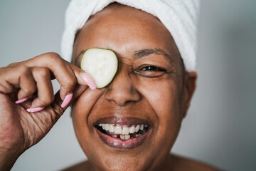 Senior african woman having fun holding cucumber skin care therapy - Main focus on eye