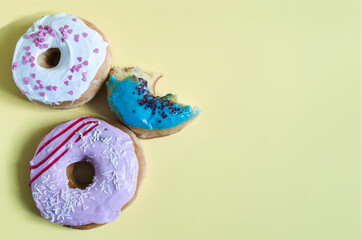 Donuts with colored glaze on a yellow background of kopi space. Colored donuts and a bitten donut on a colored background