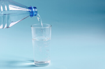 A plastic bottle that pours water into a glass glass on a colored background. A glass of clean water on a blue background close-up.
