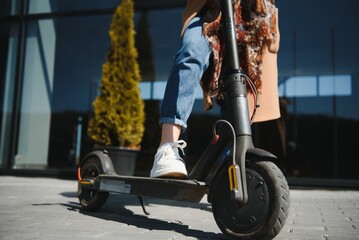 Close up of woman riding black electric kick scooter at cityscape, motion blur © Serhii