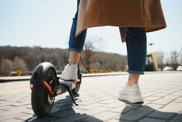 Close up of woman riding black electric kick scooter at cityscape, motion blur © Serhii