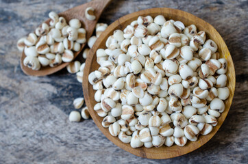 Top view of dry organic job's tear seeds in wooden bowl and spoon on grunge background. Concept of healthy food ingredient or agricultural product concept