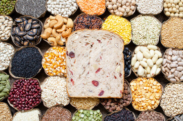 Top view of sliced homemade whole wheat and nut bread put on variety kinds of natural organic cereal and grain seed in dry banana leaf bowl on wooden background. For concept of healthy and clean food 