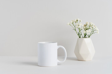 White mug mockup with beige vase and gypsophila branch on a table
