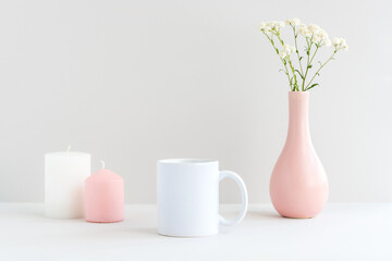 White mug mockup with candles, pink vase and gypsophila branch on a table