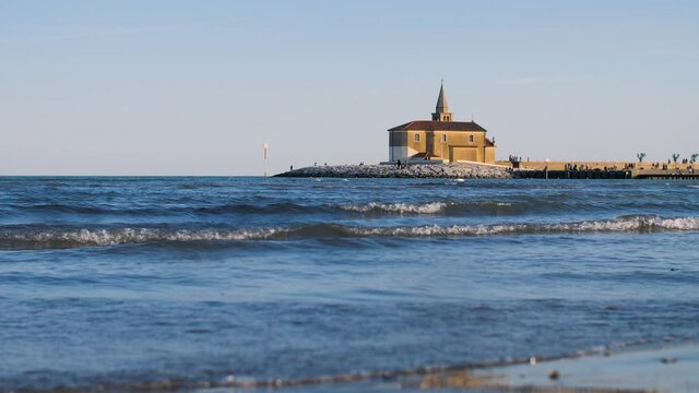 A small church on the beach in the Italian town Caorle in Veneto, Italy. The coastal Catholic chapel during sunset is a famous landmark and tourist attraction during the summer holidays. 4K.