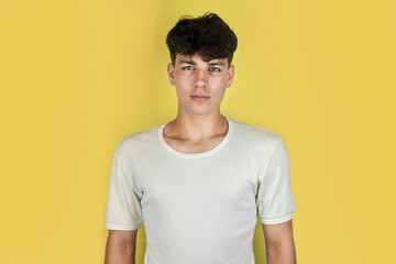Cute teenager guy in a white T-shirt on a yellow background, the guy has a serious face but he is not angry, just a little sad, something advertises